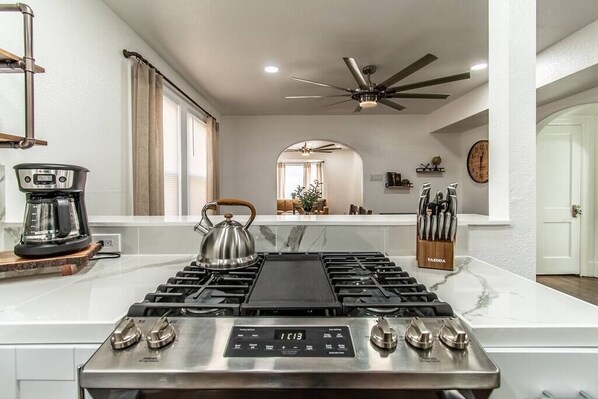 A modern kitchen with a gas stove, coffee maker, and a view of the living area.
