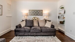 A living room with a dark grey sofa, a fluffy white rug, and a decorative wall piece.