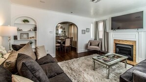 A living room with a fireplace, a television, and a dining area in the background.
