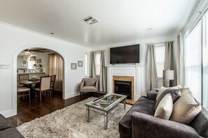 A living room with a fireplace, a TV, and a dining area visible through an archway. - Tranquil Terrace - Duplex #2 (Corpus Christi)