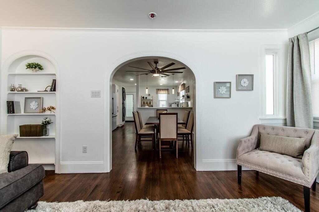 A spacious living room with a dark hardwood floor, a grey sofa, a beige armchair, and a white shag rug.
