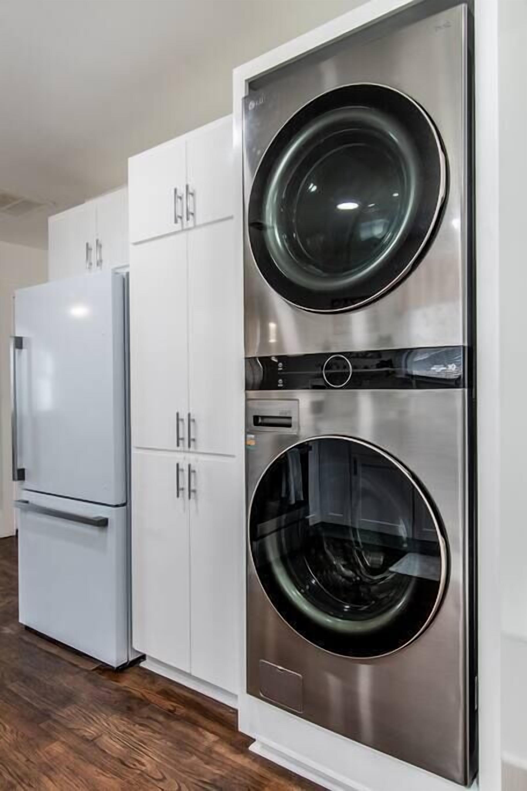 A compact kitchen with a built-in stainless steel refrigerator and a wall-mounted washer and dryer unit.