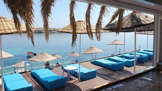 A deck with blue cushioned seating and thatched umbrellas overlooking a calm sea. - Arya Hotel Karaburun (Karaburun)