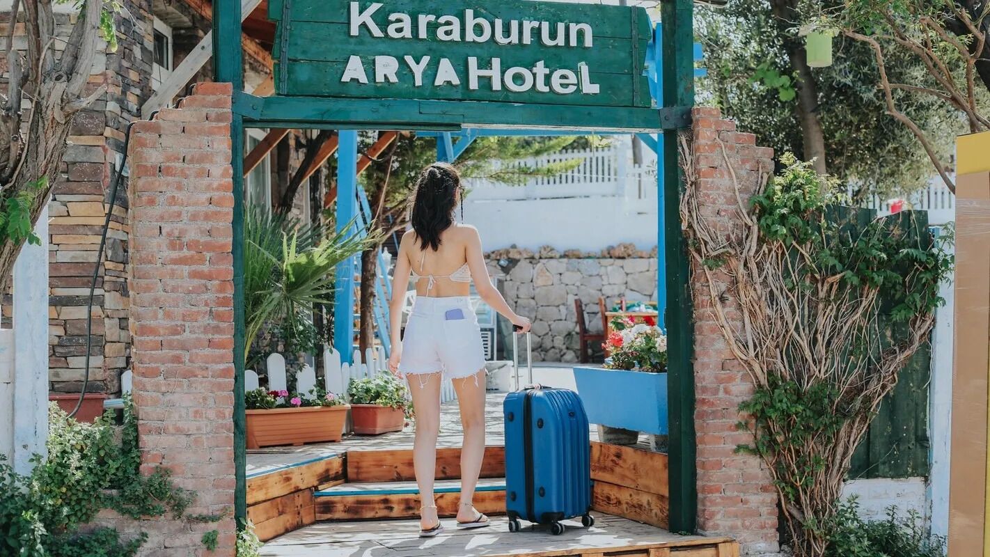 Eine Frau steht mit einem Koffer vor dem Eingang des Karaburun ARYA Hotels.