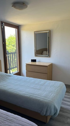 Relax in this serene bedroom with a large bed, dresser, and mirror, and step out to an outdoor space with a view of lush greenery.