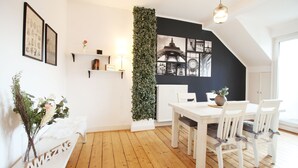A dining area with a white table and chairs, a white bench, a wall-mounted shelf with books and a lamp, and a large green vertical garden. - Boho-artstudio: Schicke Designer-wohnung mit Workspace +zentral+wifi+alexa+ (Duisburg)