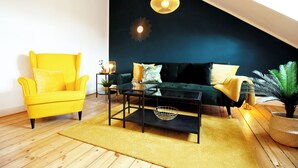 A modern living room with a yellow armchair, a dark green sofa, a glass coffee table, and a black floor lamp. - Boho-artstudio: Schicke Designer-wohnung mit Workspace +zentral+wifi+alexa+ (Duisburg)