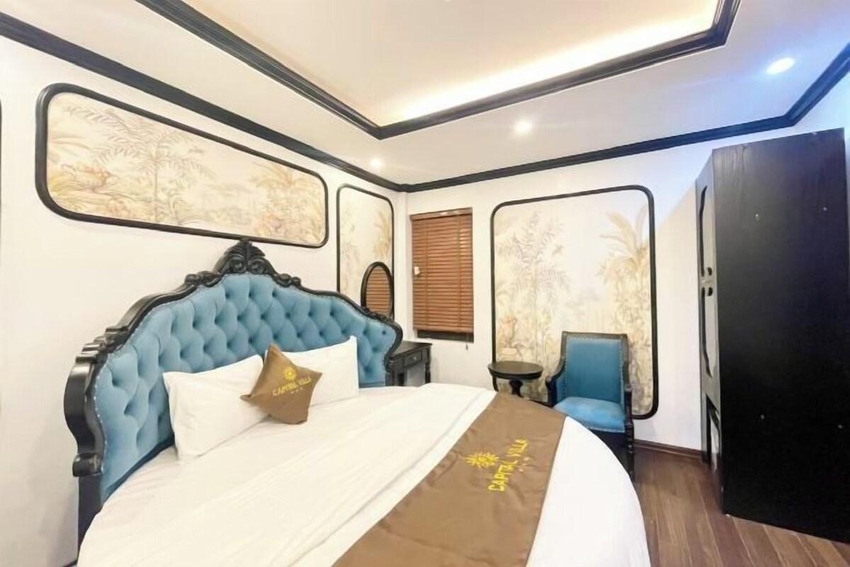 A bedroom with a tufted headboard, a bed with white bedding, a brown throw, a blue chair, and a wardrobe.