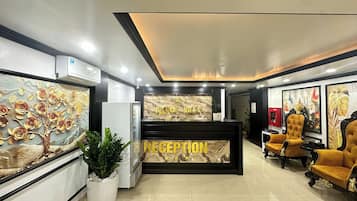 Una zona d'entrada amb un taulell de recepció de marbre, una paret amb un mural d'un arbre i una zona d'estar amb cadires tapissades.