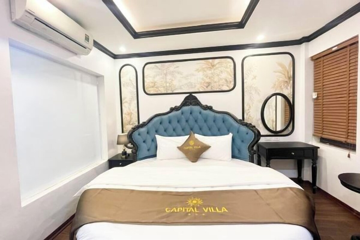 A hotel room with a large bed, a nightstand, a mirror, and a window with blinds.