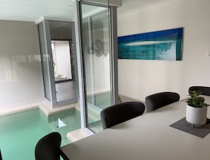A modern meeting room with a glass partition, a view of a pool, and a painting of a beach scene. - Tropical Villa Hideaway (Trinity Park)