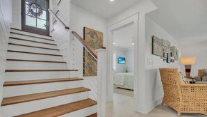 Un escalier avec des marches en bois et des murs blancs, menant à une chambre à coucher équipée d’un lit et d’un téléviseur.