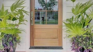 Une porte d’entrée en bois avec un panneau de verre, flanquée de deux lanternes fixées au mur, et un paillasson devant le porche.