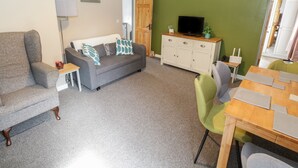 Una sala de estar con un sofá gris, un mueble de madera con un televisor y una pared verde con cuadros.
