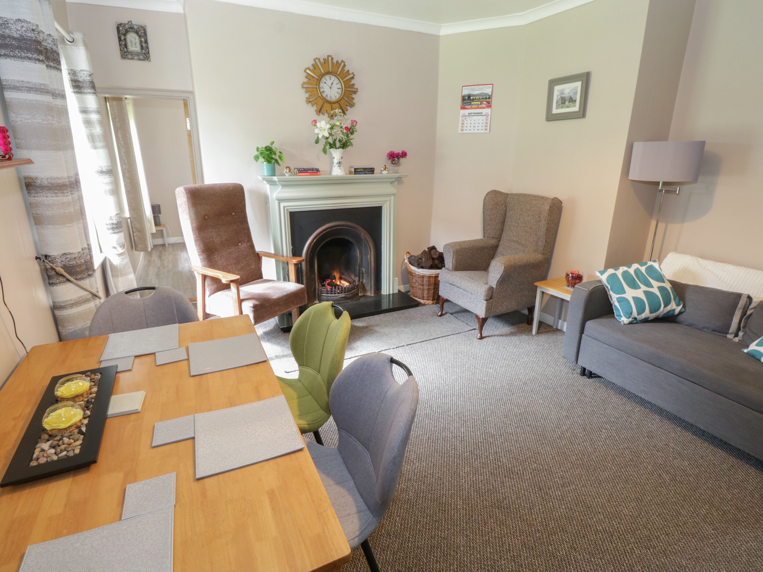 A living room with a fireplace, a sofa, a dining table with placemats, and a green chair.