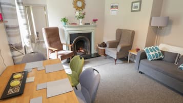 Un salon avec une cheminée, un canapé, une table à manger avec des sets de table et un fauteuil vert.