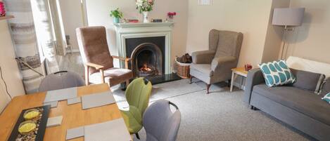 A living room with a fireplace, a sofa, a dining table with placemats, and a green chair.