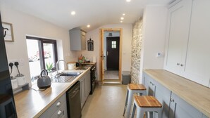 A modern kitchen with a central island, built-in appliances, and a stone accent wall. - Kate's Cottage (Ballintober)