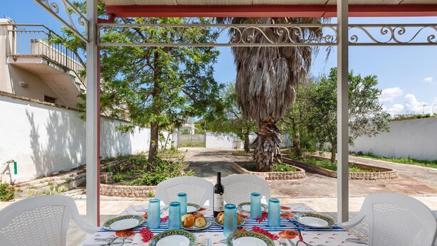Ein Essbereich im Freien mit einem Tisch für zwei Personen, umgeben von weißen Stühlen, unter einer Pergola.