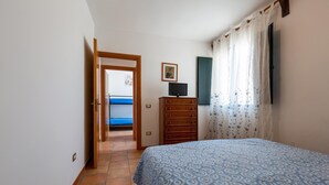 Ein Schlafzimmer mit einem Bett, einem Schminktisch, einem Fernseher und einer Tür zu einem anderen Raum.
