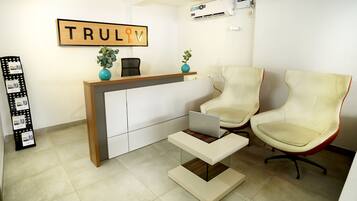 A reception area with a wooden desk, two beige chairs, a laptop, and a framed sign above the desk.