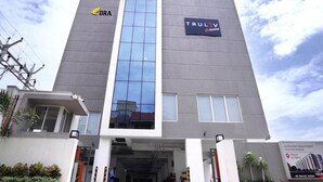 A modern building with a prominent glass facade, a logo for 'DRA' on the left, and 'TRULV' on the right. - Truliv Olympus Elite (Chennai)