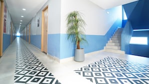 A hallway with patterned flooring, a potted plant, and a staircase with blue walls. - Truliv Olympus Elite (Chennai)
