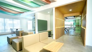 A modern office space with a large sofa, a small table, and a conference area with chairs and a table. - Truliv Olympus Elite (Chennai)
