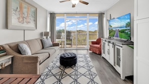 A living room with a sofa, ottoman, TV, and a ceiling fan. - Seaside Elegance Your Coastal Getaway (North Myrtle Beach)