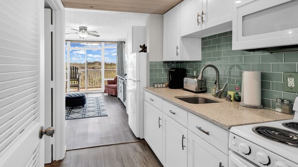 A kitchen with white cabinets, a stove, and a sink. - Seaside Elegance Your Coastal Getaway (North Myrtle Beach)