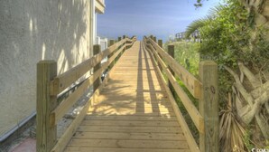 A wooden boardwalk leading to a building with a white exterior wall. - Seaside Elegance Your Coastal Getaway (North Myrtle Beach)