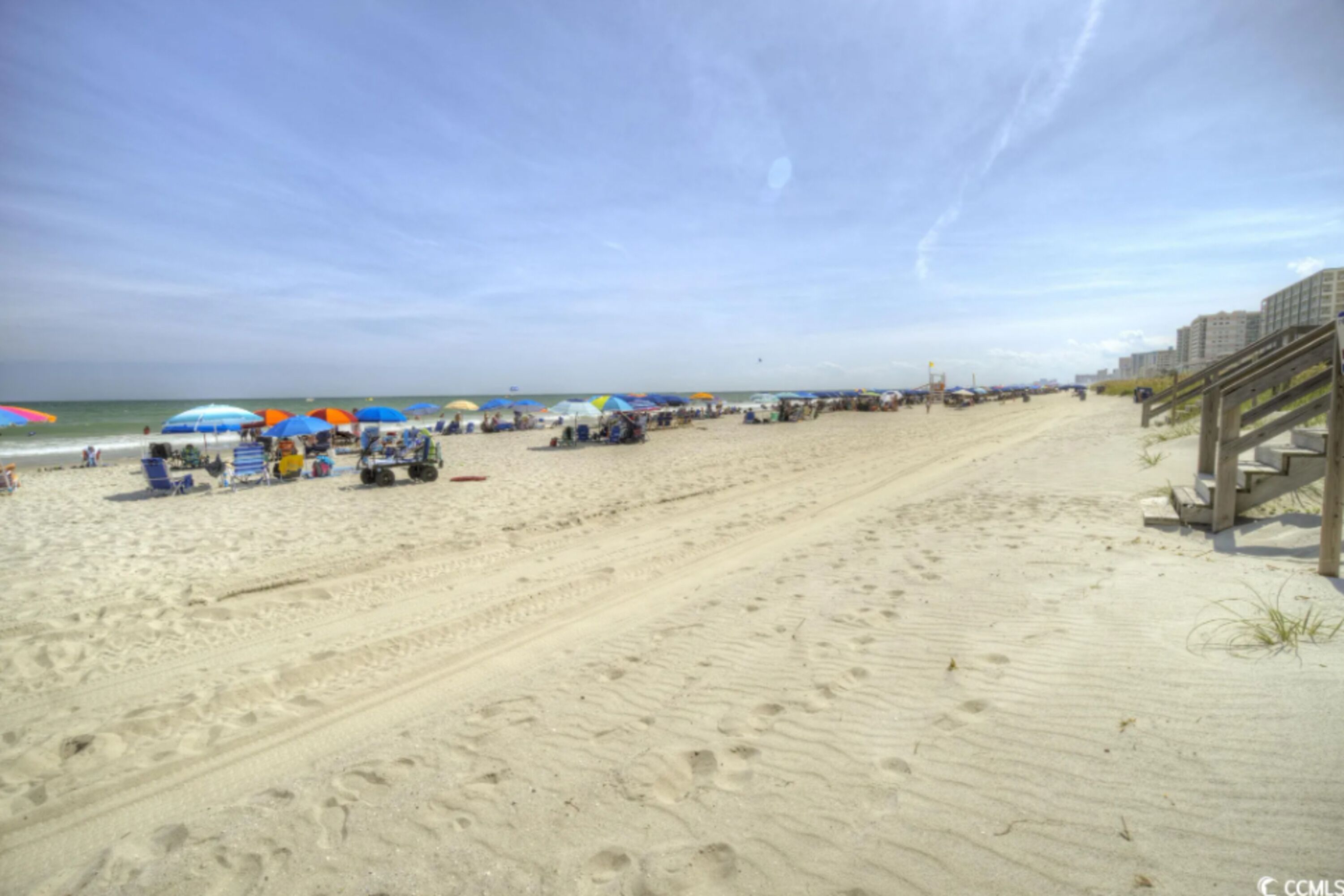 Een zandstrand met parasols en ligbedden, een houten loofpad en een heldere lucht.