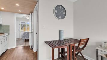A kitchen with wooden cabinets, a dining table with chairs, a wall clock, and a ceiling fan.