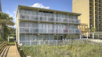 Een meerhoog hotel met balkons, een houten boardwalk en een gazon ervoor.