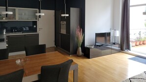 A modern kitchen with dark cabinetry, a dining area with a wooden table and chairs, and a large window with a view of the outdoors.