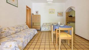 A compact room with a bed, a small table with a tablecloth, a chair, a kitchenette, and a door leading to another room. - 3447 Villetta Grazia by Barbarhouse (Nardò)