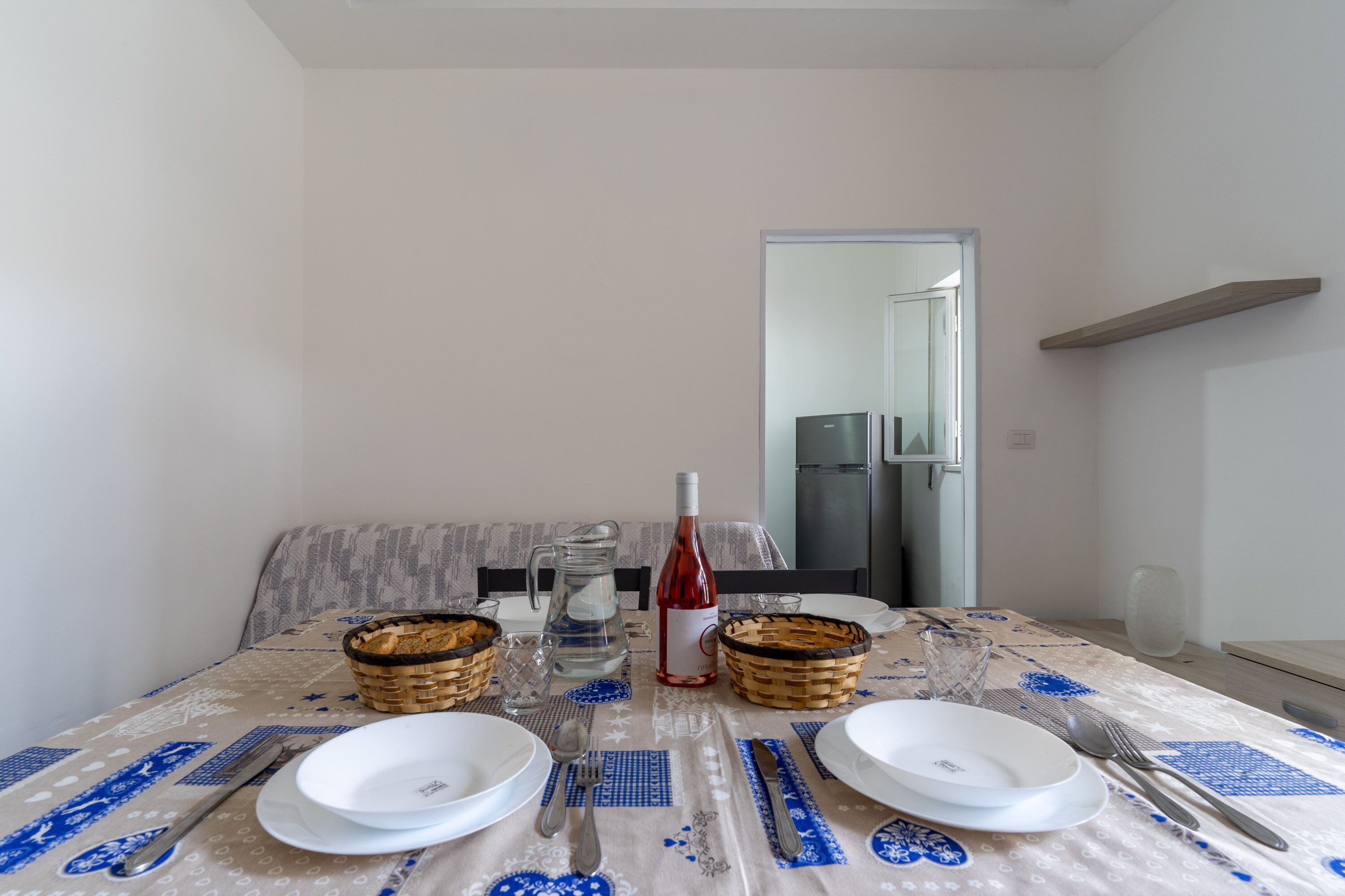 A dining table set with plates, cutlery, a wine bottle, and baskets.