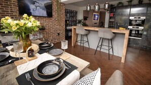 A modern kitchen with a bar area, a dining table set with plates and cutlery, and a TV mounted on a brick wall. - The Longsands Home • Coastal w/ Hot Tub (Tynemouth)