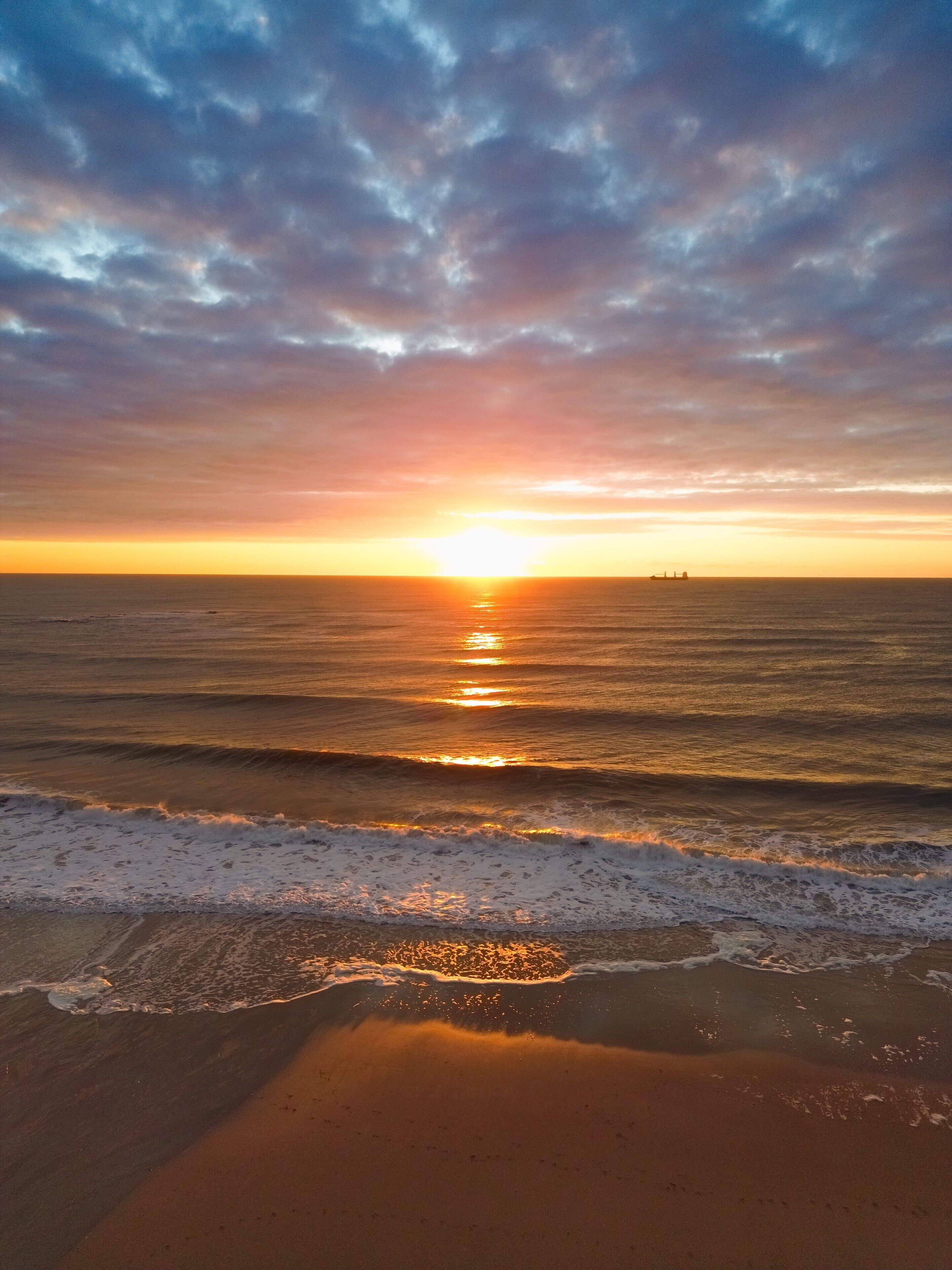A beach with waves and a sunset.