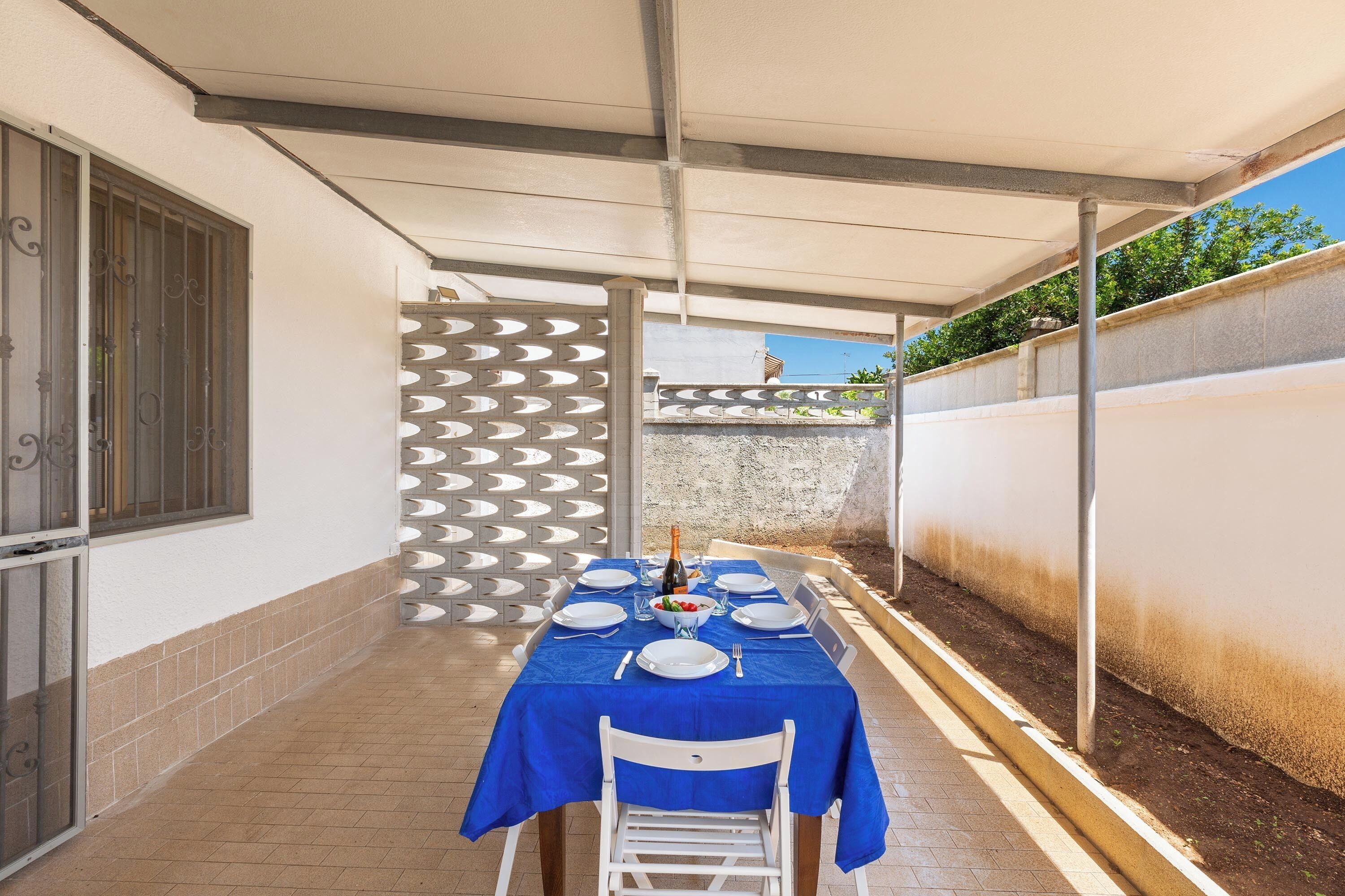 A covered outdoor dining area with a table set for four, a bottle of champagne, and a decorative wall.