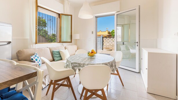 A compact living space with a dining area, a sofa, a glass door leading outside, and a small kitchenette. - 3592 Villetta Ninì by Barbarhouse (Porto Cesareo)