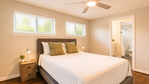 Une chambre à coucher avec un lit, des tables de chevet, un ventilateur de plafond et une vue sur la salle de bain.