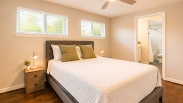 Une chambre à coucher avec un lit, des tables de chevet, un ventilateur de plafond et une vue sur la salle de bain.