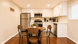 Une cuisine avec des meubles blancs, un réfrigérateur en acier inoxydable, un four à micro-ondes, une cuisinière et un lave-vaisselle. On y trouve une table ronde en bois, accompagnée de quatre chaises.