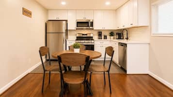Une cuisine avec des meubles blancs, un réfrigérateur en acier inoxydable, un four à micro-ondes, une cuisinière et un lave-vaisselle. On y trouve une table ronde en bois, accompagnée de quatre chaises.
