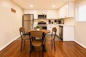 A kitchen with white cabinets, a stainless steel refrigerator, a microwave, a stove, and a dishwasher. There is a round wooden table with four chairs.