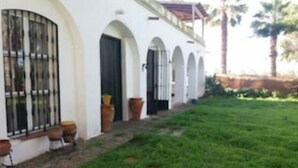 Un edifici blanc amb portals i finestres d'arc, un pati enjardinat i plantes en testos.