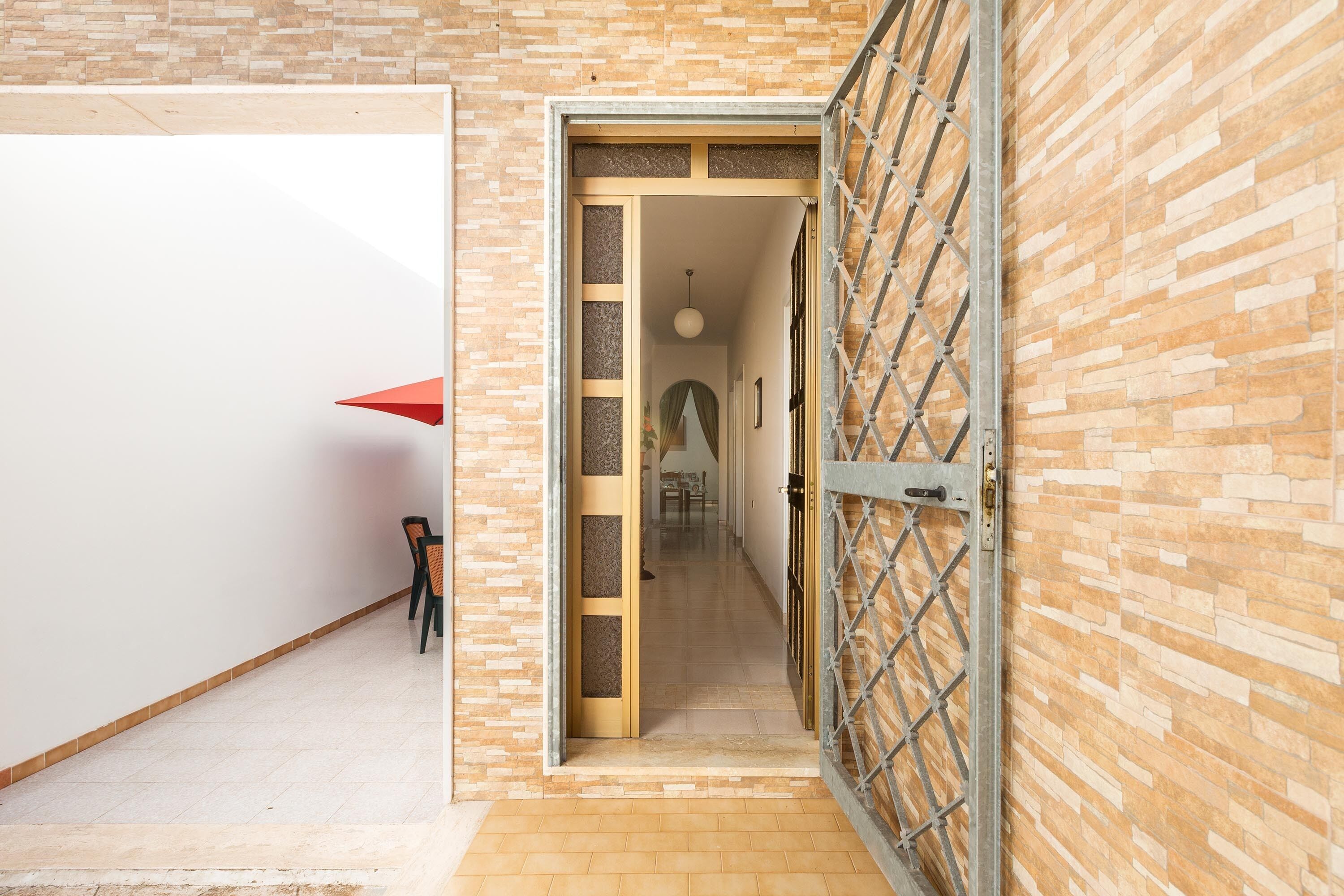 A hallway with a brick wall and a metal gate leading to another room.
