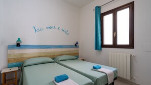 Ein Schlafzimmer mit zwei Betten, einem Holzkopfteil, einem Fenster mit Vorhängen und einer Wand mit einer italienischen Schrift.