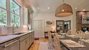 Une cuisine moderne dotée d’une grande fenêtre, d’un plancher en bois et d’un coin repas avec un mur en pierre et un luminaire suspendu.